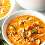 Top down view white bowl with creamy sausage and tortellini soup. The large pot of soup is off to the side.