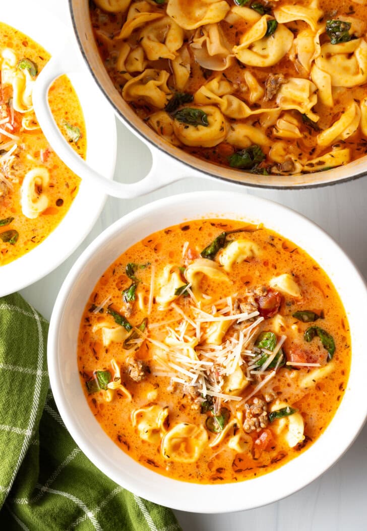 Top down view white bowl with creamy sausage and tortellini soup. The large pot of soup is off to the side.