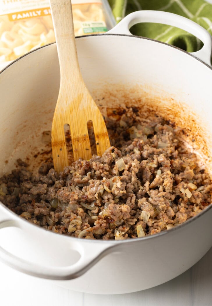 White large cooking pot with ground browned sausage and wooden spoon.