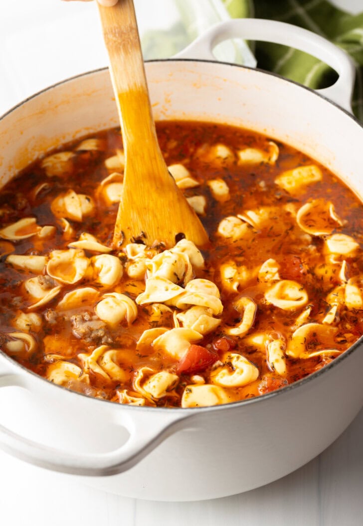 Brown spatula stirring soup in a large white pot.