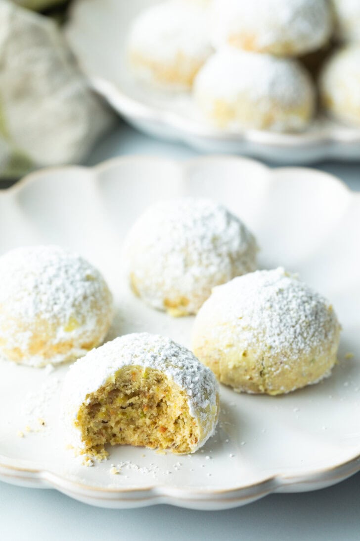 4 wedding cookies dusted with powdered sugar, the closest cookie to camera has a bite taken out.