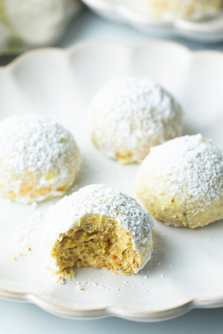 4 wedding cookies dusted with powdered sugar, the closest cookie to camera has a bite taken out.