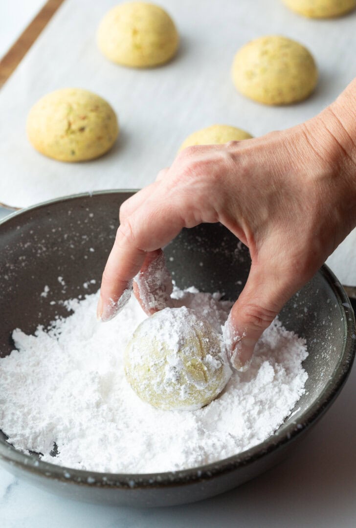 Hand rolling a round cookie in a bowl of powdered sugar.