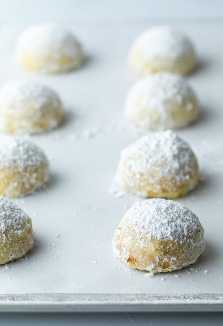 Several wedding cookies on a baking sheet, dusted with powdered sugar.