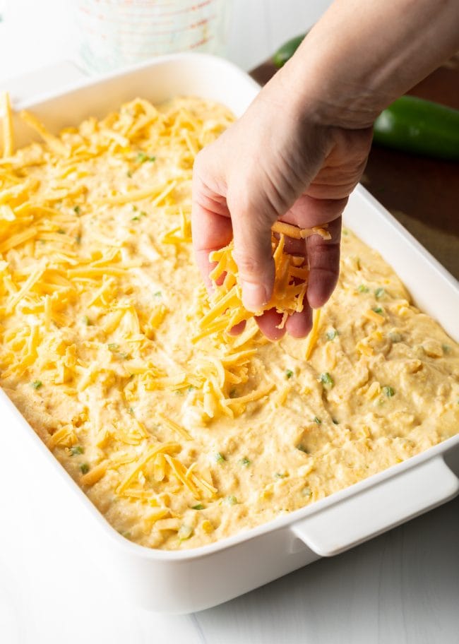 adding shredded cheese to the top of the unbaked batter in a casserole dish