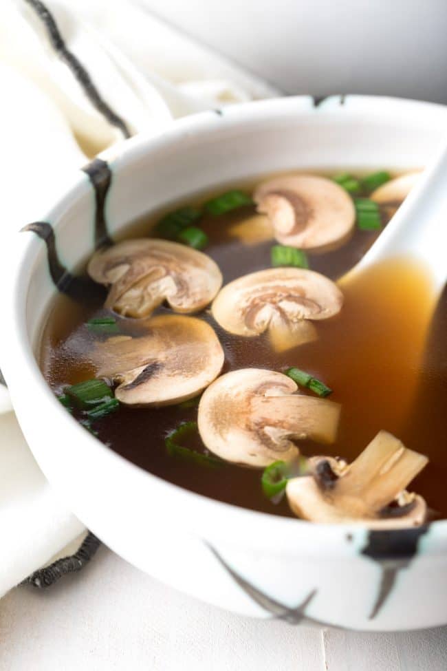 Bowl of healthy clear soup with mushrooms and scallions and a large soup spoon.