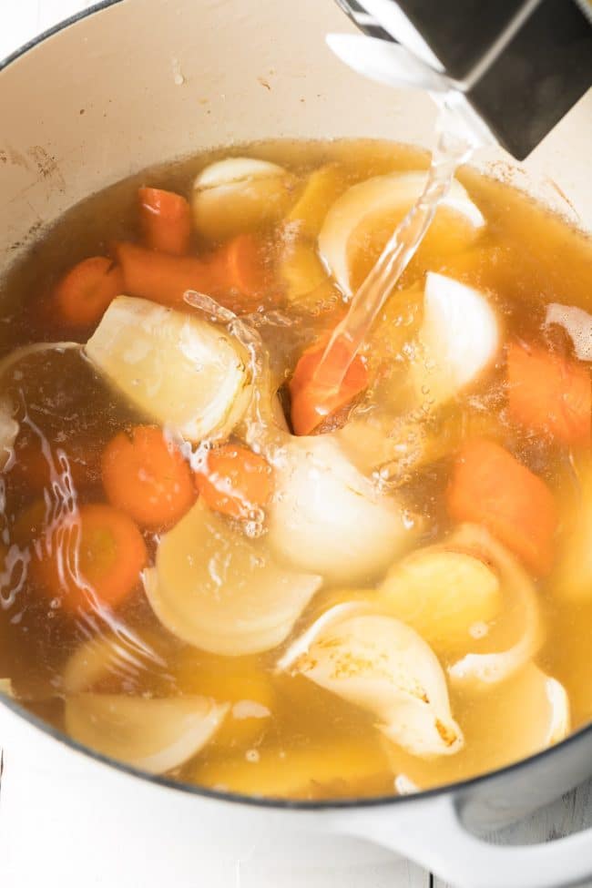 Water being poured into the pot over the veggies. 