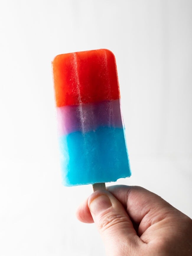 Hand holding up rainbow popsicle.