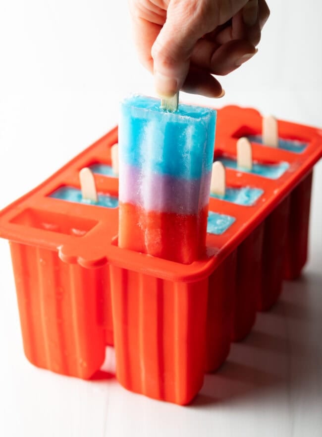 Hand pulling a blue, purple, red rainbow popsicle from mold.