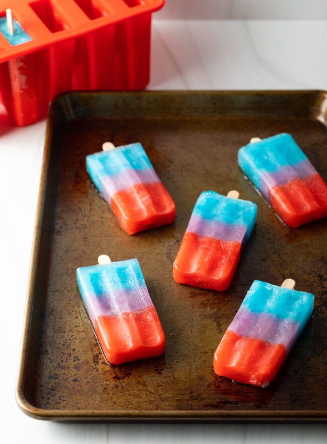 5 rainbow popsicles on a rimmed baking sheet.