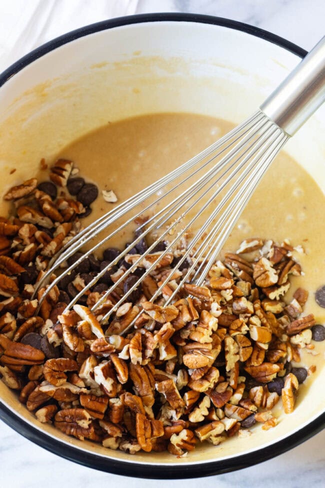 Whisking chopped nuts and chocolate chips into an eggy batter in a large mixing bowl.