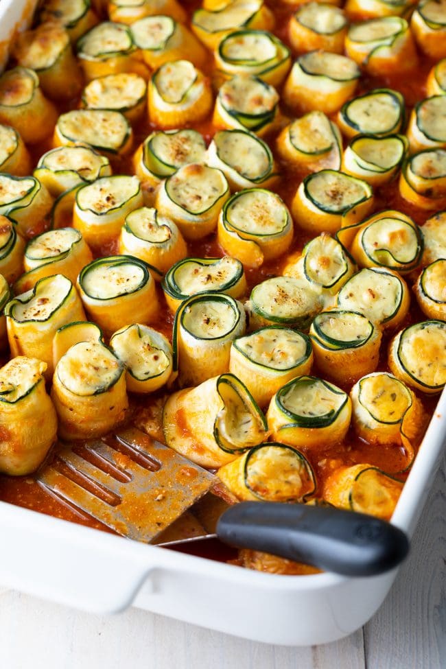 keto zucchini lasagna roll ups in a baking dish with a spatula in the dish. 