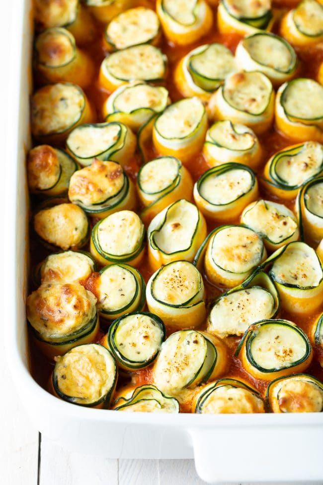 low carb keto zucchini roll ups in a white baking dish.