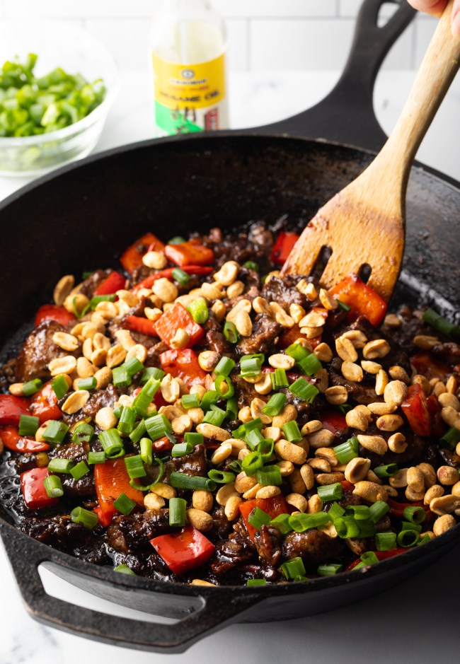 Wooden spoon stirring spicy stir fry beef in a cast iron skillet.