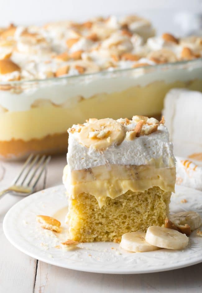 Slice of banana pudding cake on a white plate with more cake in the background. 