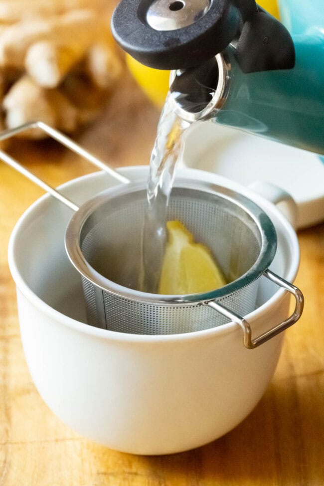 Pouring hot water over the lemon and ginger in a tea infuser in a mug.