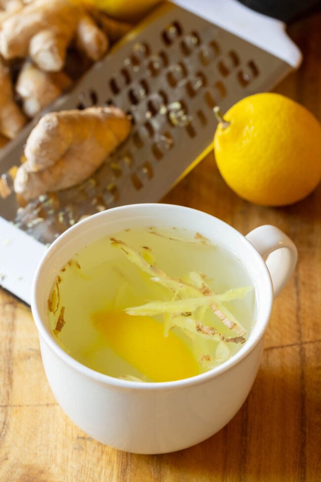 Lemon ginger tea in a white mug with ginger and lemon in the background. 