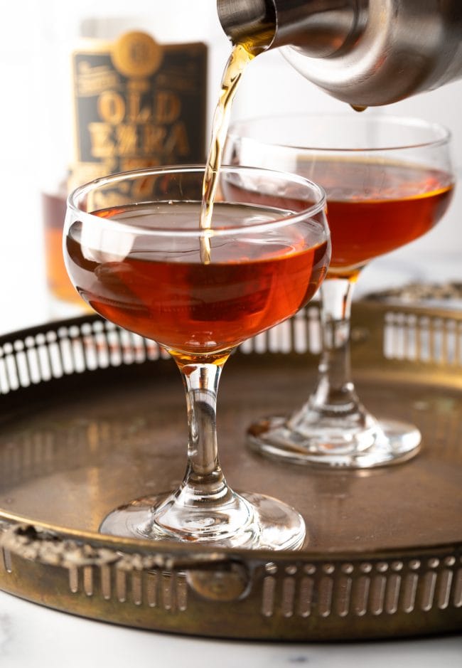 Perfect Manhattan Recipe being poured from a shaker into a coupe glass. 