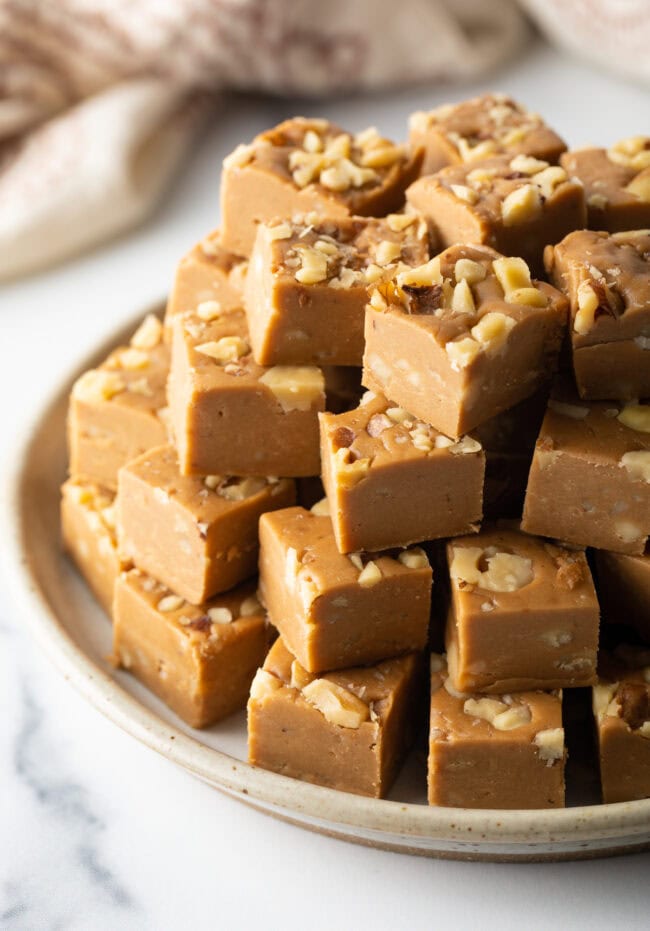 Beautiful plate of maple fudge squares with walnuts stacked up similar to a pyramid.