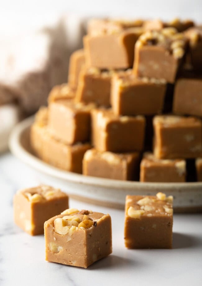 Squares of maple walnut fudge in front of a stack of fudge.