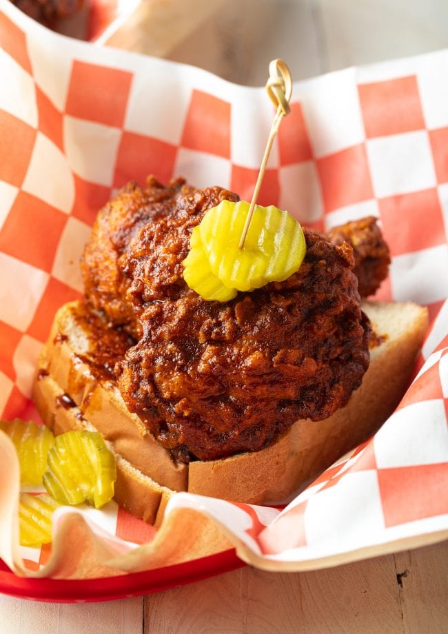 Nashville hot chicken recipe in a basket on white bread with pickles on top. 