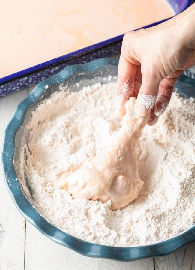 Hand dipping chicken legs in flour to fry. 