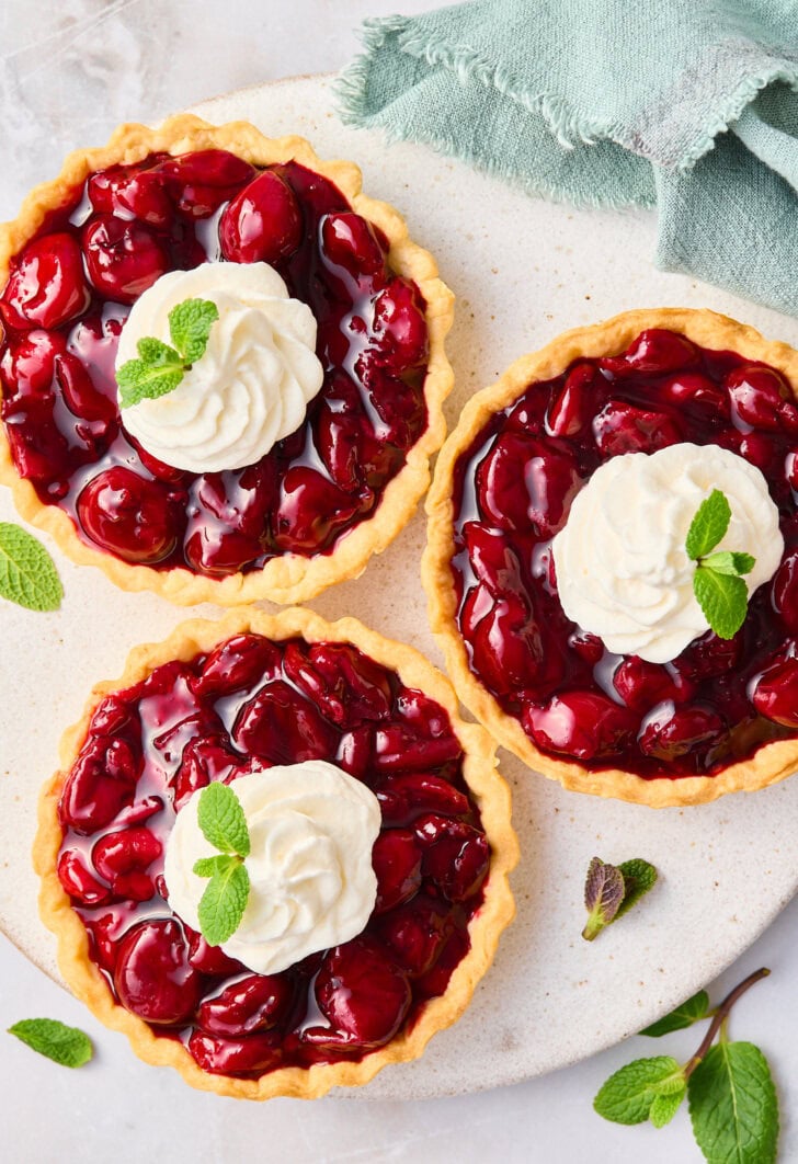 Overhead shot of three cherry tarts topped with whipped cream and mint. 