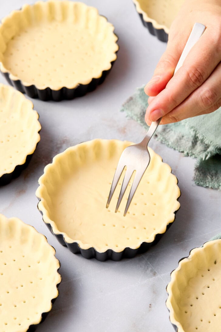 Hand using a fork to poke holes in the bottom of the pie crust in the tart pan. 