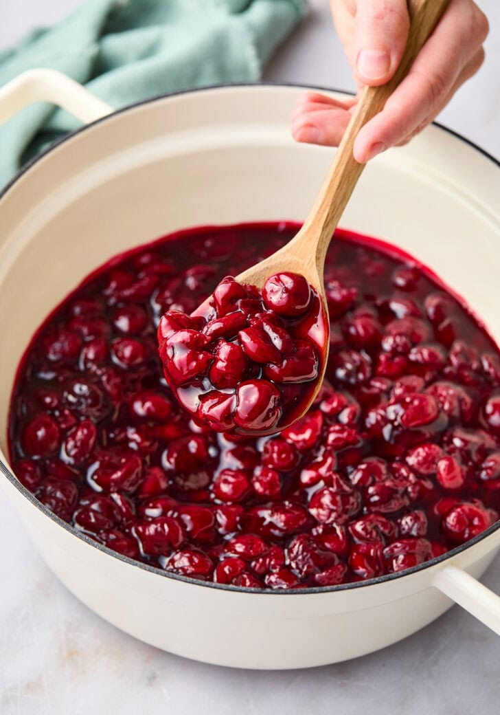 Cherry pie mixture in a large pot with a wooden spoon scooping some up. 