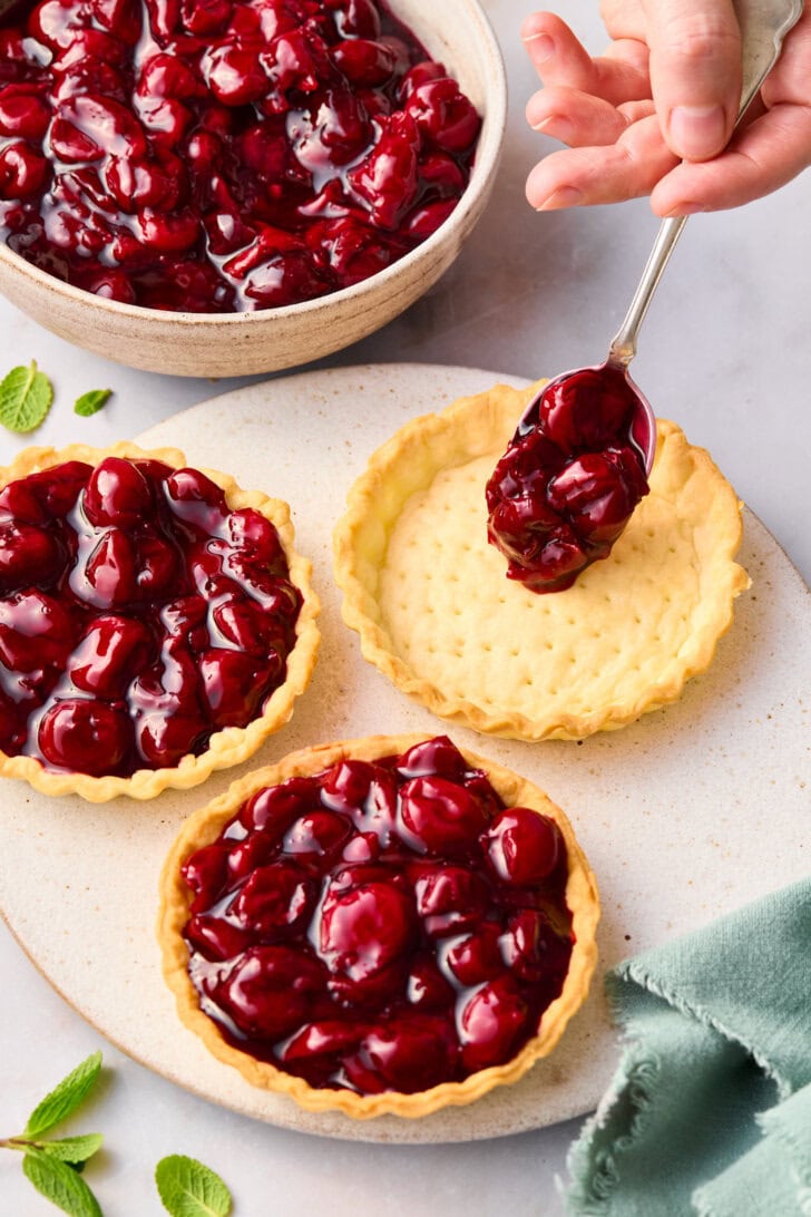 Filling mini cherry pie crusts with fruit filling.