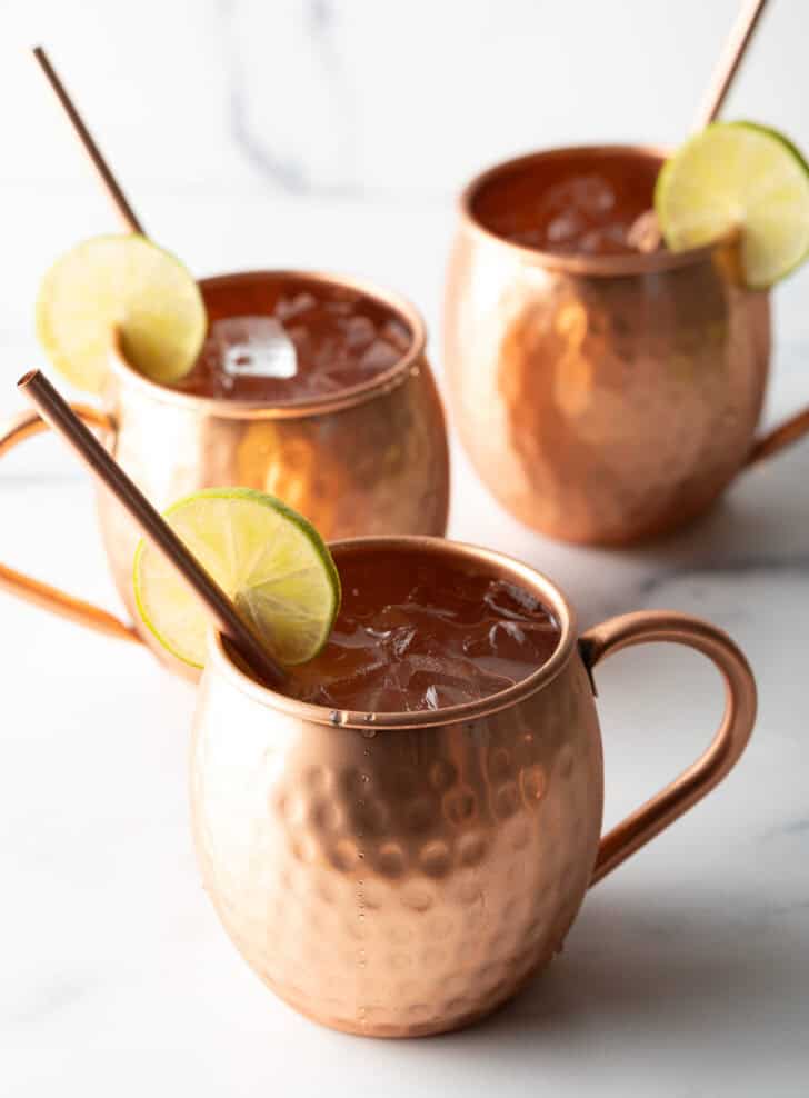 Best Moscow Mule Recipe - 3 moscow mules in copper mugs, each with a copper metal straw and slice of lime on the rim.