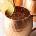 Close view of a moscow mule in a copper handled mug, with a copper metal straw and slice of lime to garnish the rim.