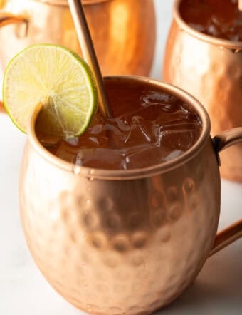 Close view of a moscow mule in a copper handled mug, with a copper metal straw and slice of lime to garnish the rim.