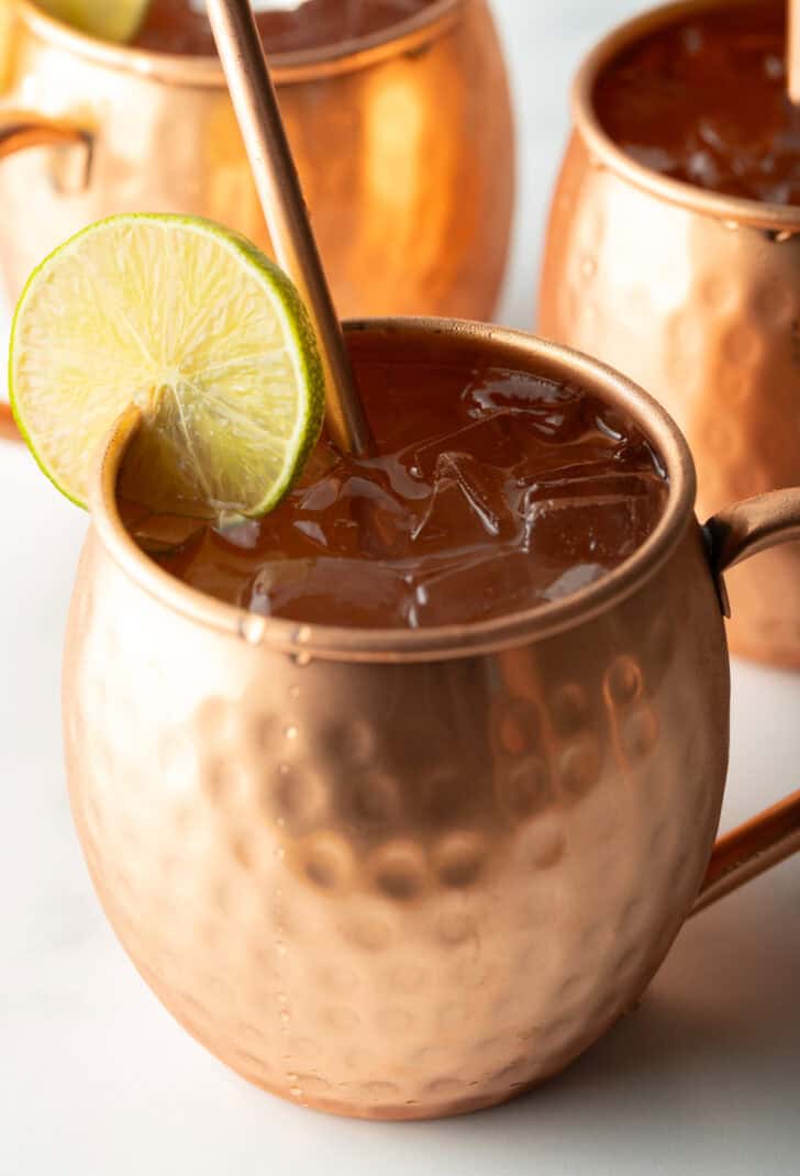 Best Moscow Mule Recipe - Close view of a moscow mule in a copper handled mug, with a copper metal straw and slice of lime to garnish the rim.