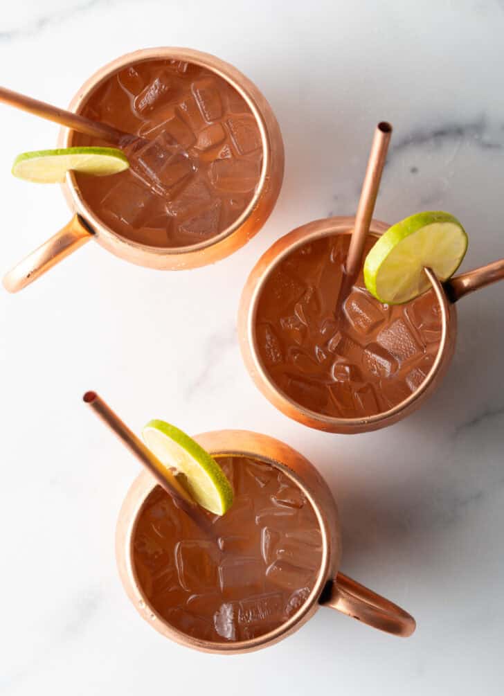 Top down view 3 bronze mugs with metal straws and a garnish of lime slice on the rim.