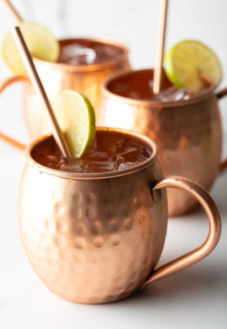 Close view of a moscow mule in a copper handled mug, with a copper metal straw and slice of lime to garnish the rim.