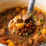 Ladleful of Mulligan stew with chopped potatoes, carrots, peas, and chunks of beef.