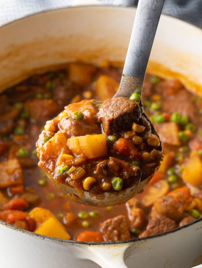 Ladleful of Irish Stew with chopped potatoes, carrots, peas, and chunks of beef.