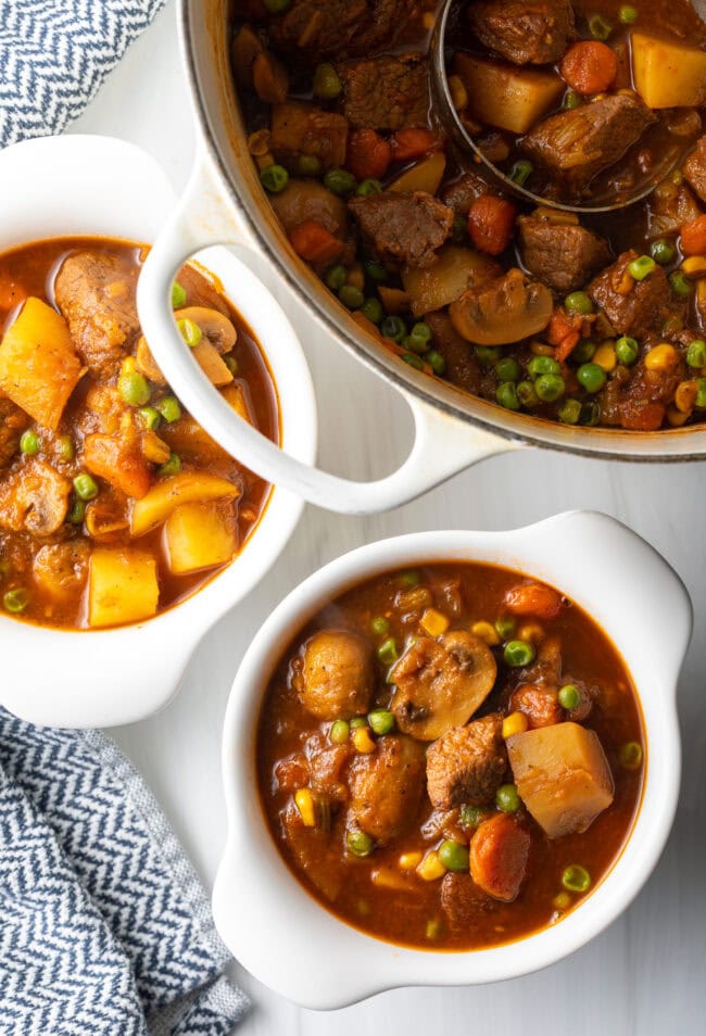 Top down Mulligan stew with chopped potatoes, carrots, peas, and chunks of beef in two white bowls.