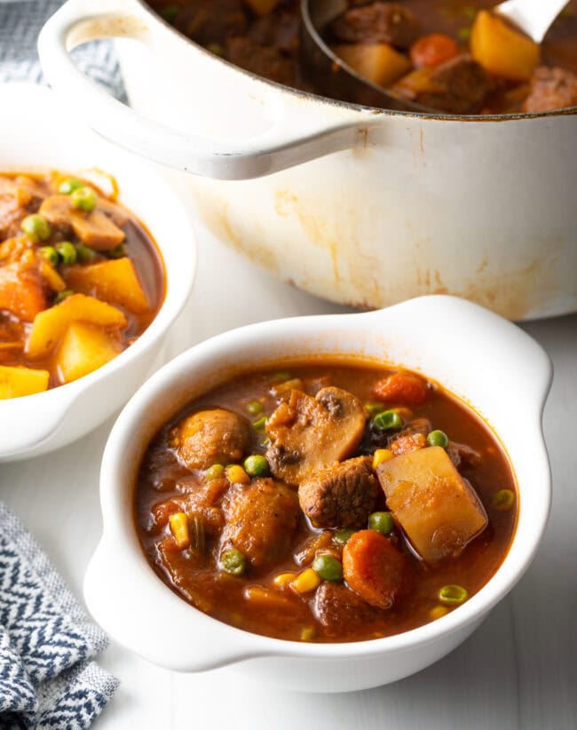 Hobo stew with chopped potatoes, carrots, peas, and chunks of beef in two white bowls.