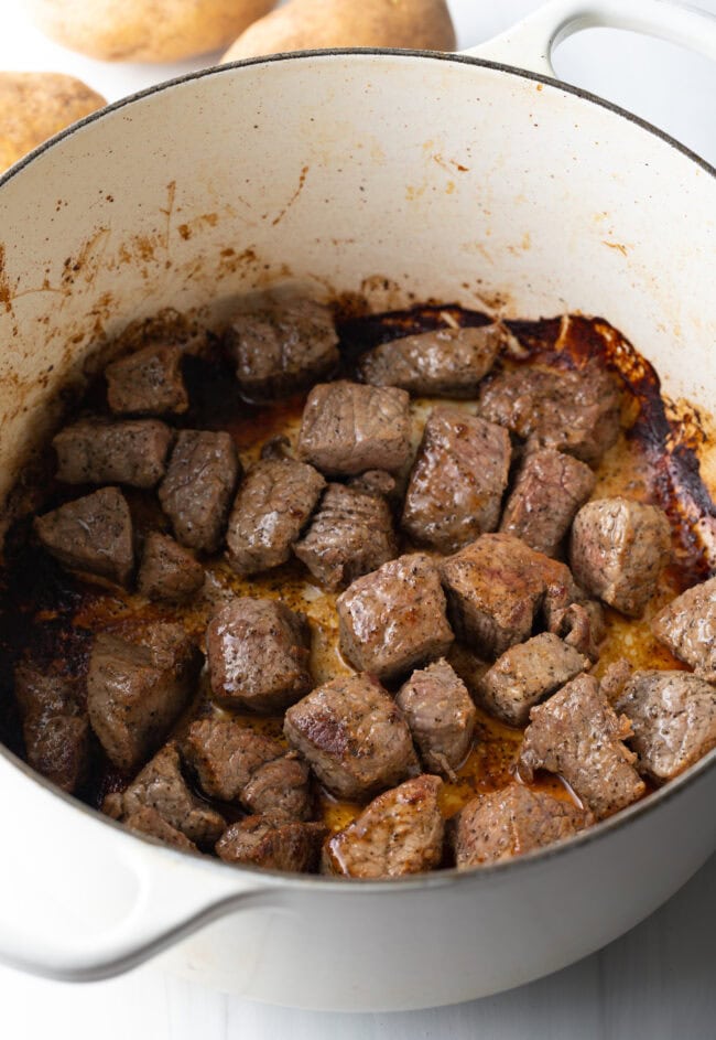 Chunks of stew meat cooking on the stove top in a dutch oven.