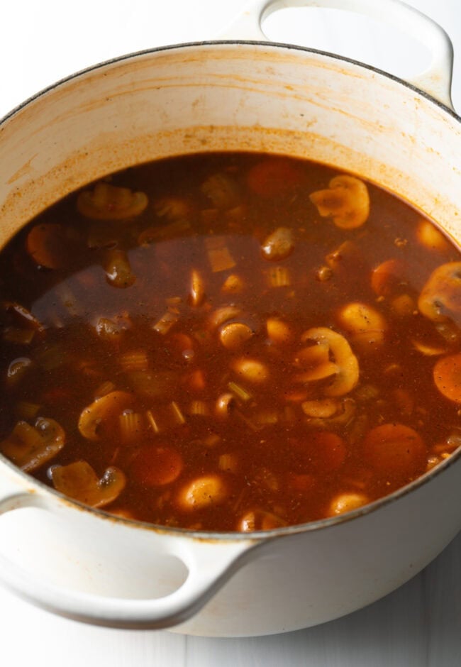 Adding mushrooms and in a tomato broth in a pot.