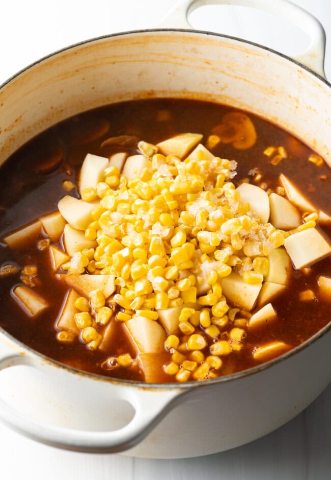 Adding potatoes and garlic in a tomato broth in a pot for hobo stew