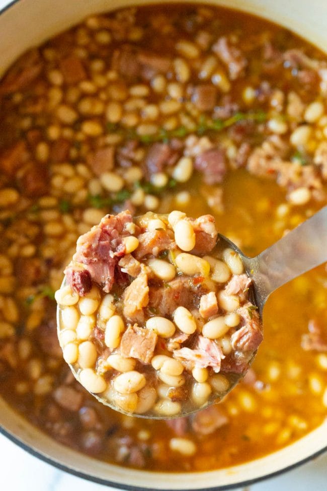 Ladle full of soup above a full pot fresh off the stove 
