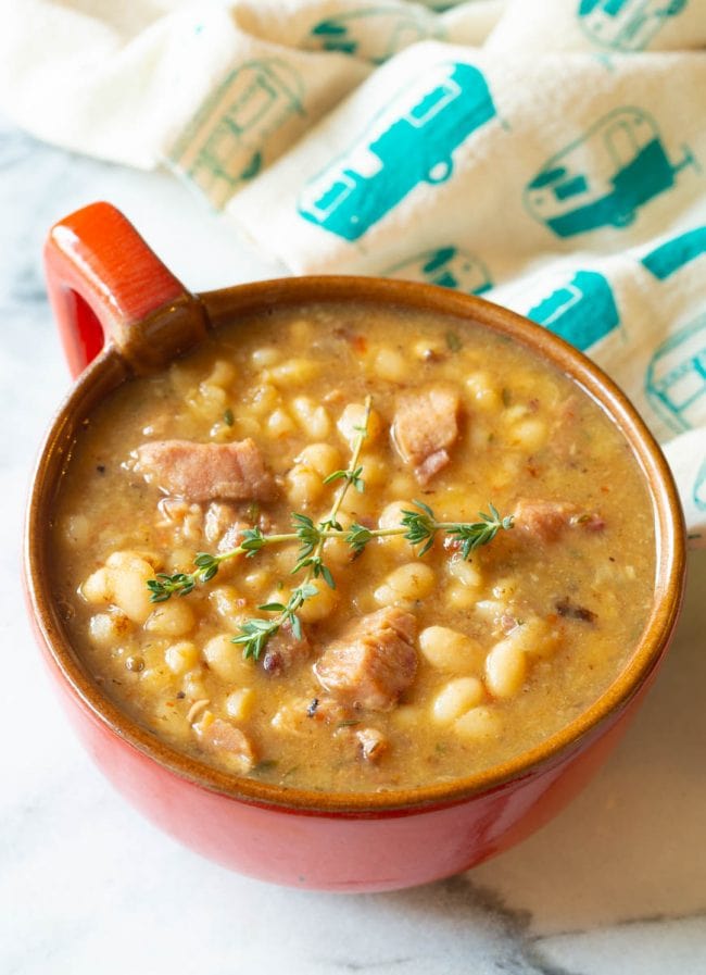 Red bowl with a handle filled with navy bean soup with ham. 