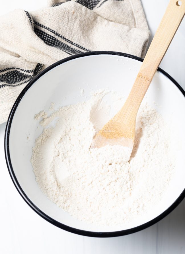 Dry ingredients in a mixing bowl with a wooden spoon.