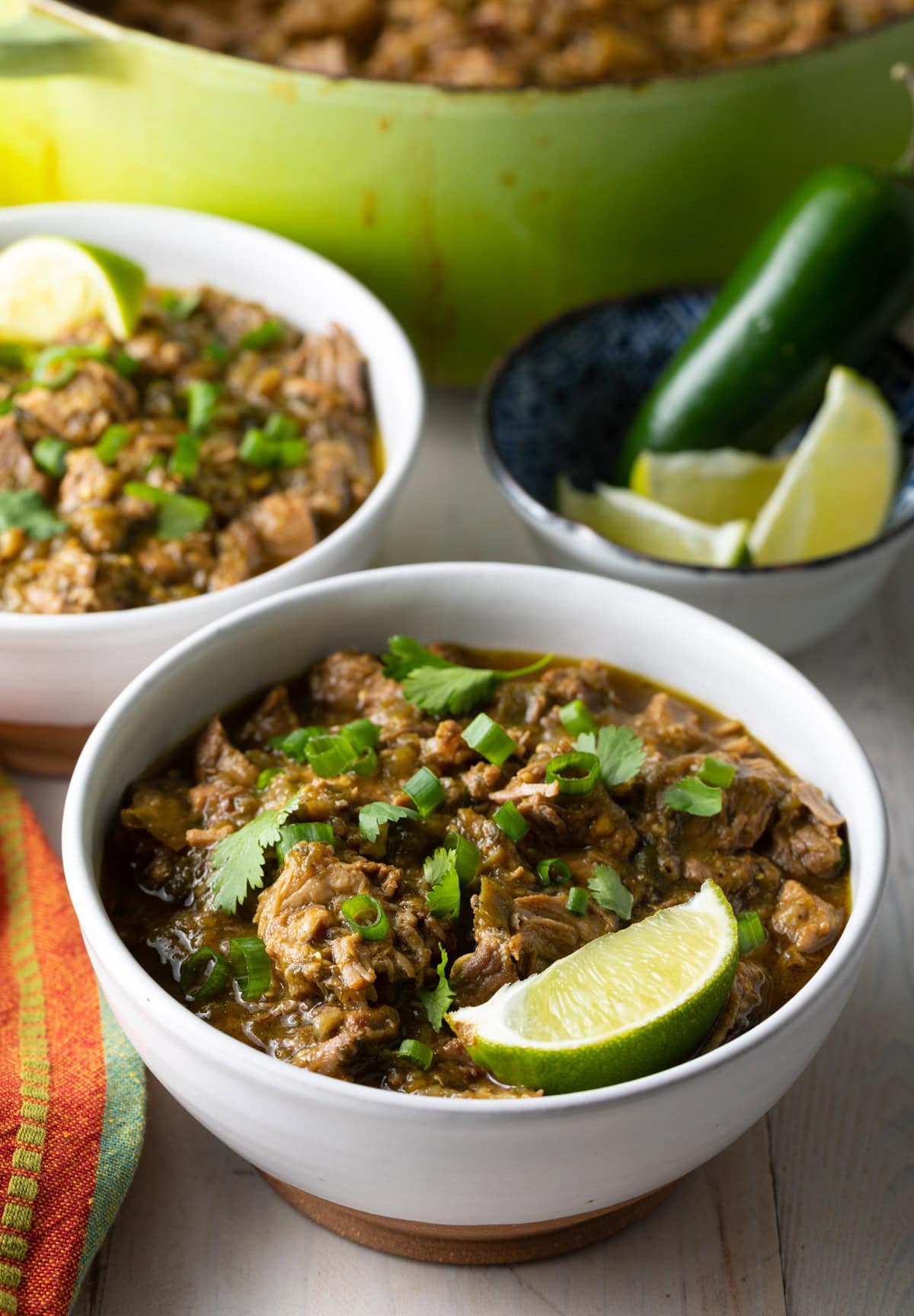 Two bowls of Green Chili (Chile Verde) with lime wedges on the side. 