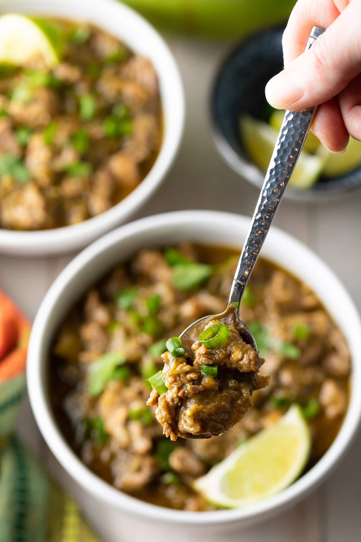 Authentic pork green chile with a spoon holding a bite above a bowl. 