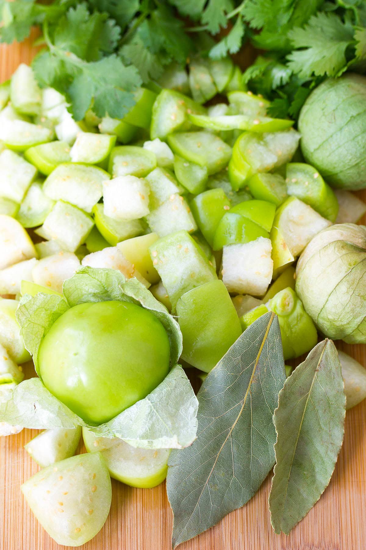 Diced tomatillos on a cutting board with cilantro and bay leaves. 