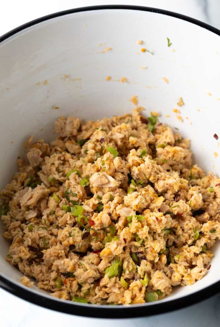 Flaked salmon with breadcrumbs and herbs in a white mixing bowl.